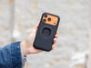 Hand in a denim jacket holding the MAG case with an all-black ring, orange camera plate showing at the top
