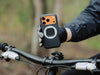 Cyclist lifts an iPhone in the MAG case with a white ring over a mountain bike&